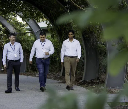 NAIF Staff CEO Craig Doyle Indigenous Outcomes Director Darren Chong And Senior Associate Jamari Buli Talking As They Walk Through A Green Park In Cairns