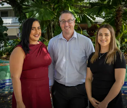 Leanne Tullemans, Stuart Pres and Helen Santolin from the Cairns Investment team posing for a photo in front of Indigenous mosaic and lush tropical garden