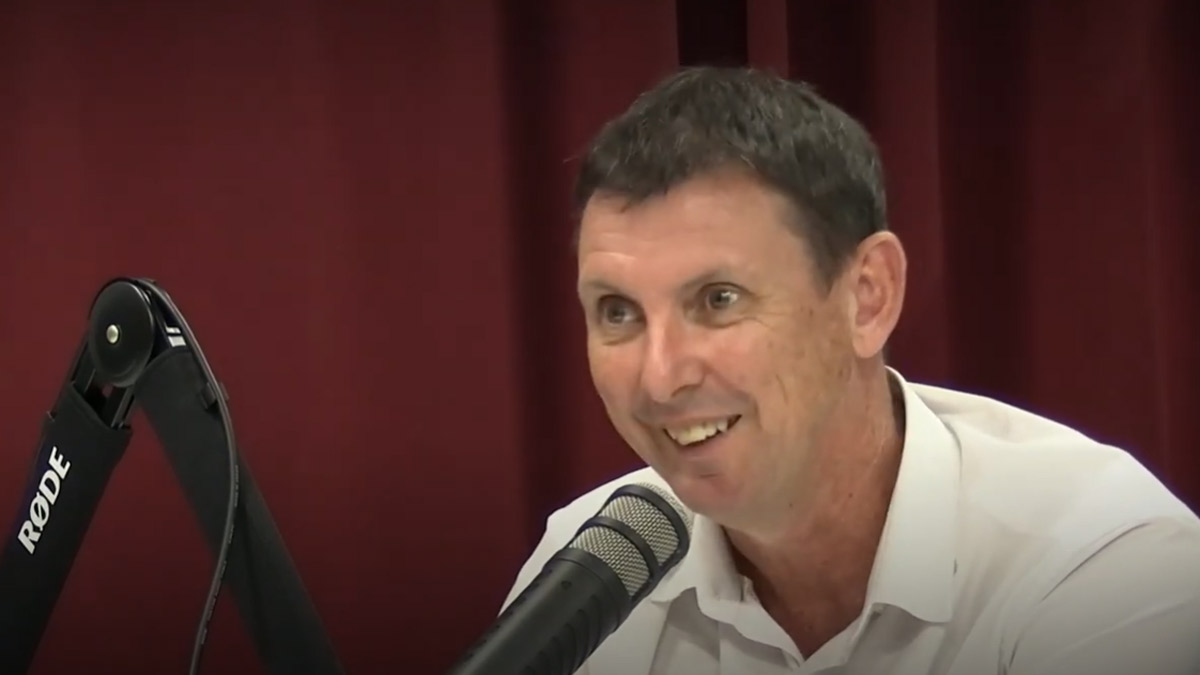Craig Doyle speaking into microphone with red curtain background