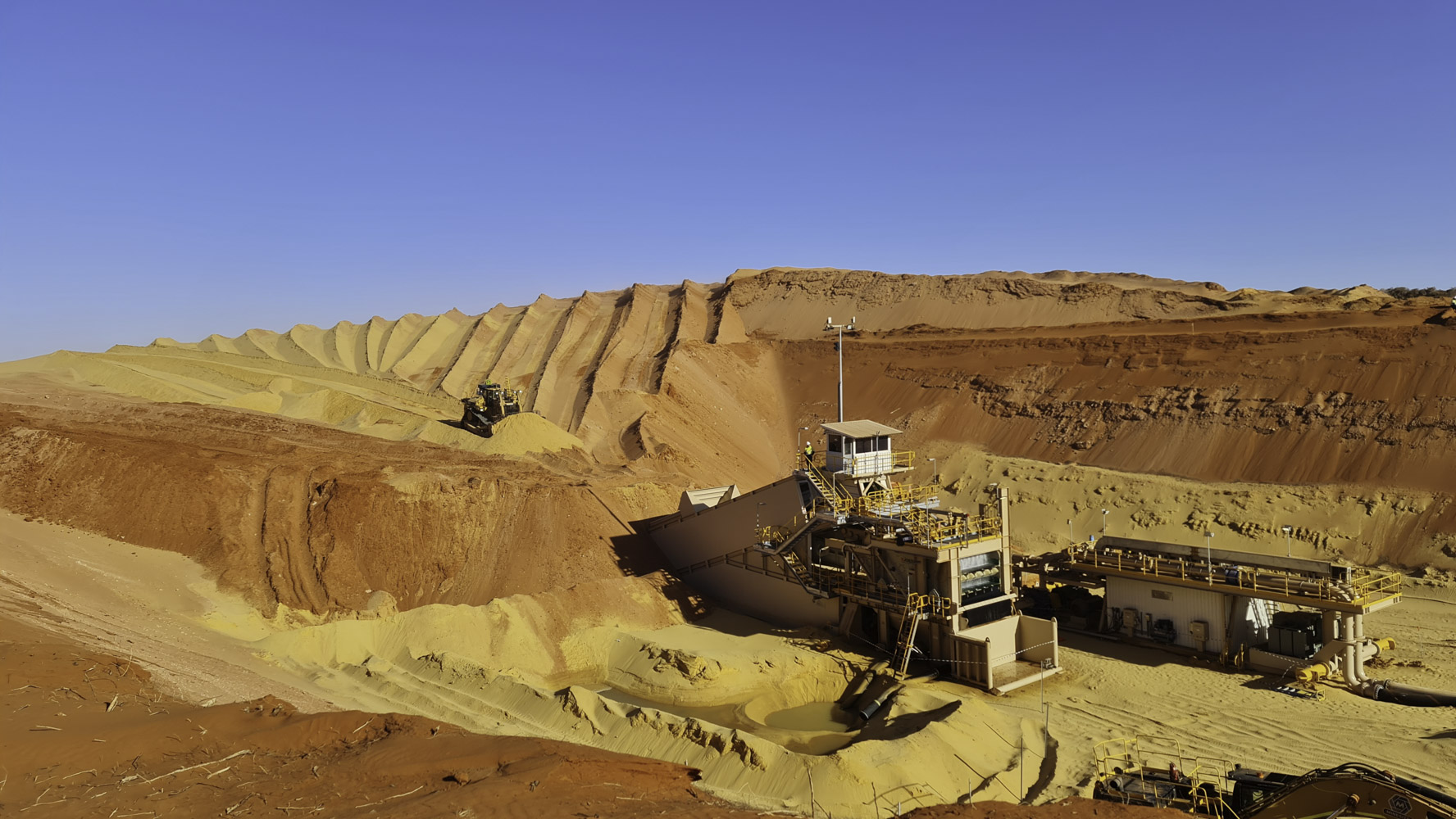 Strandline Resources Coburn Heavy Mineral Sands Project Wide View Of Mine Pit With Excavator Pushing Yellow Soil Into A Building