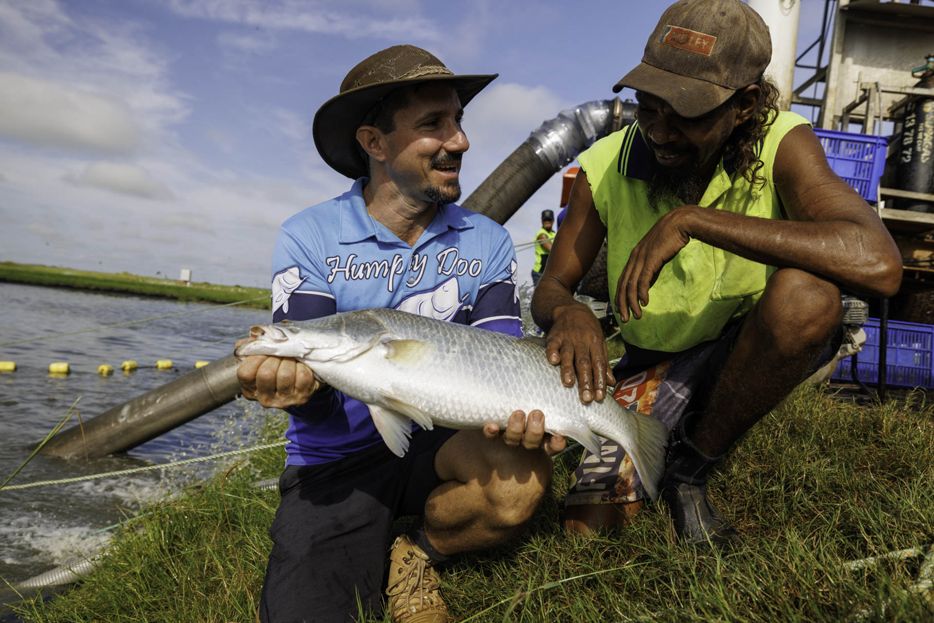 Humpty Doo Barramundi CEO Holding A Large Barramundi With And Indigenous Employee At The Side Of A Pond (1)