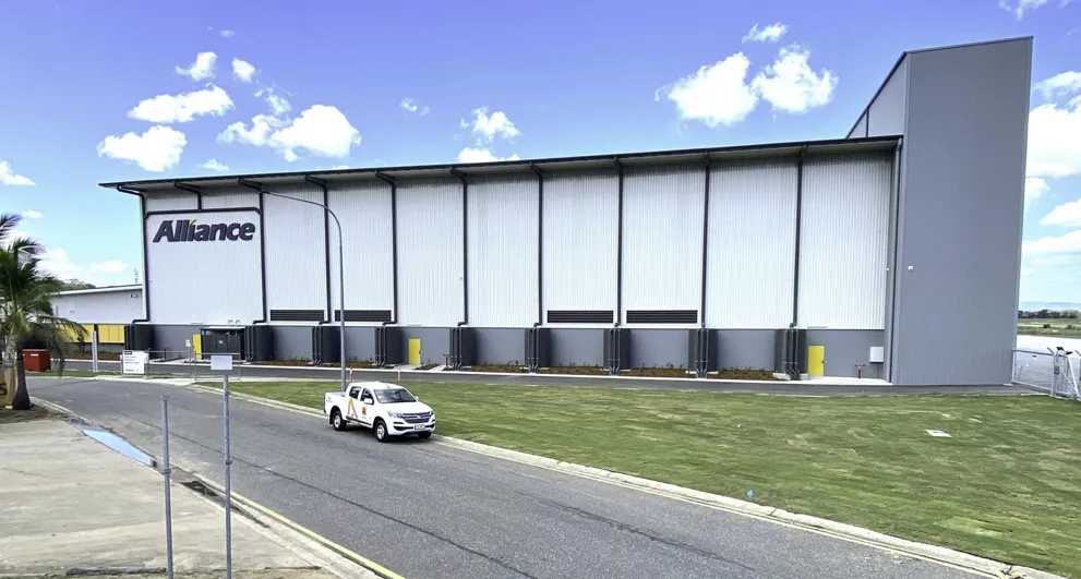 Alliance Airlines Transport and Logistics hangar with white sheet metal sidings and grey pillars with a road and a car in the foreground