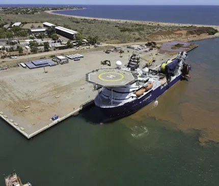 Onslow Marine Support Base Aerial View Of Blue And White Ship With Helipad Docked To Base With Coastline And Ocean In Background on Onslow Marine Support Base
